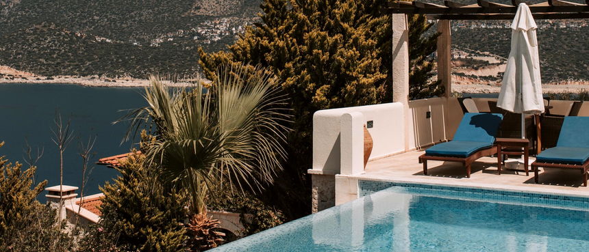 A villa pool with sun loungers above a blue bay