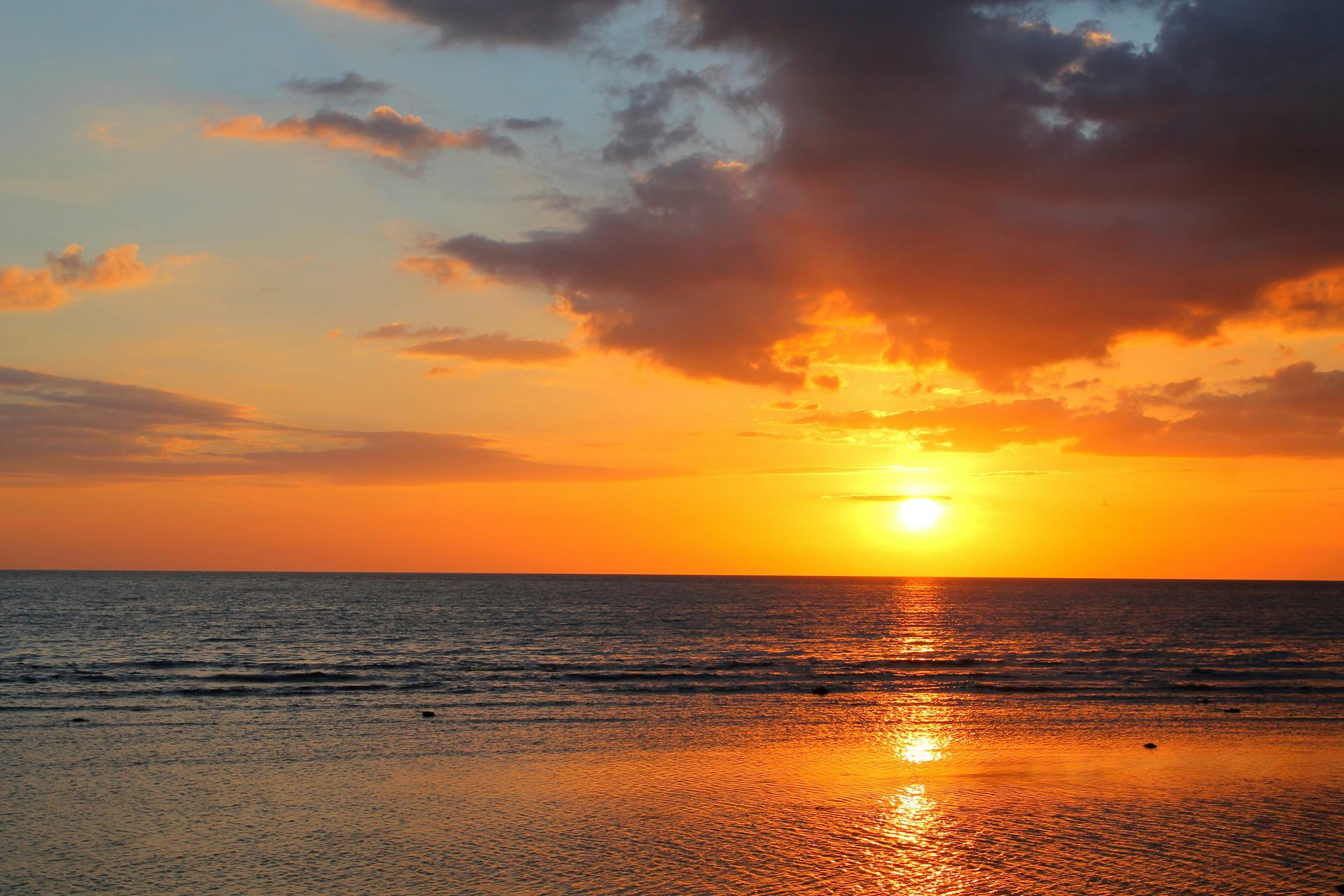 The sun setting over a calm sea off Bali, orange sky and a gold path on the water