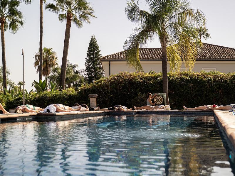 Guests resting on loungers beside the villa pool, palms behind