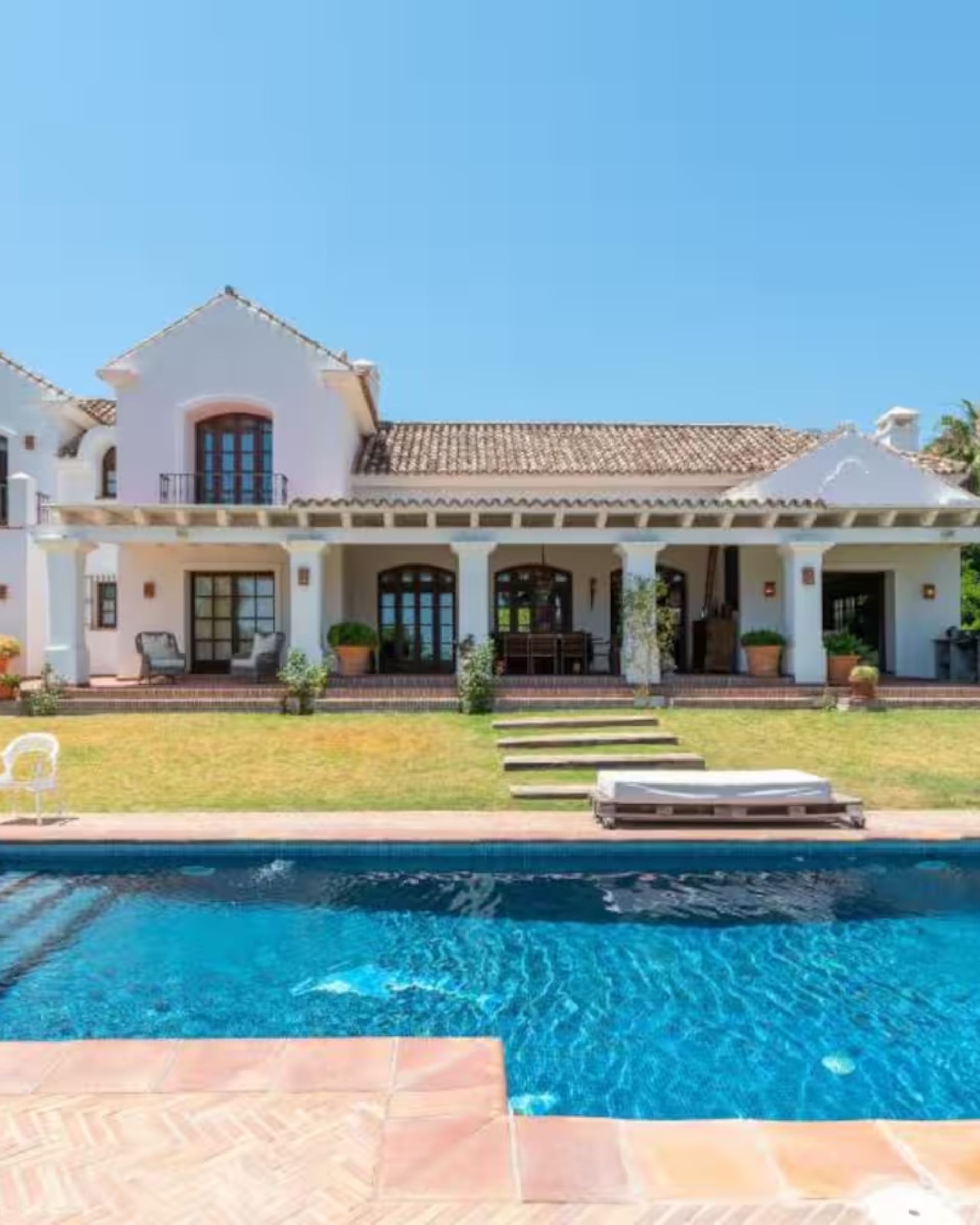 White Andalusian villa with a large pool and lawn under a blue sky in southern Spain