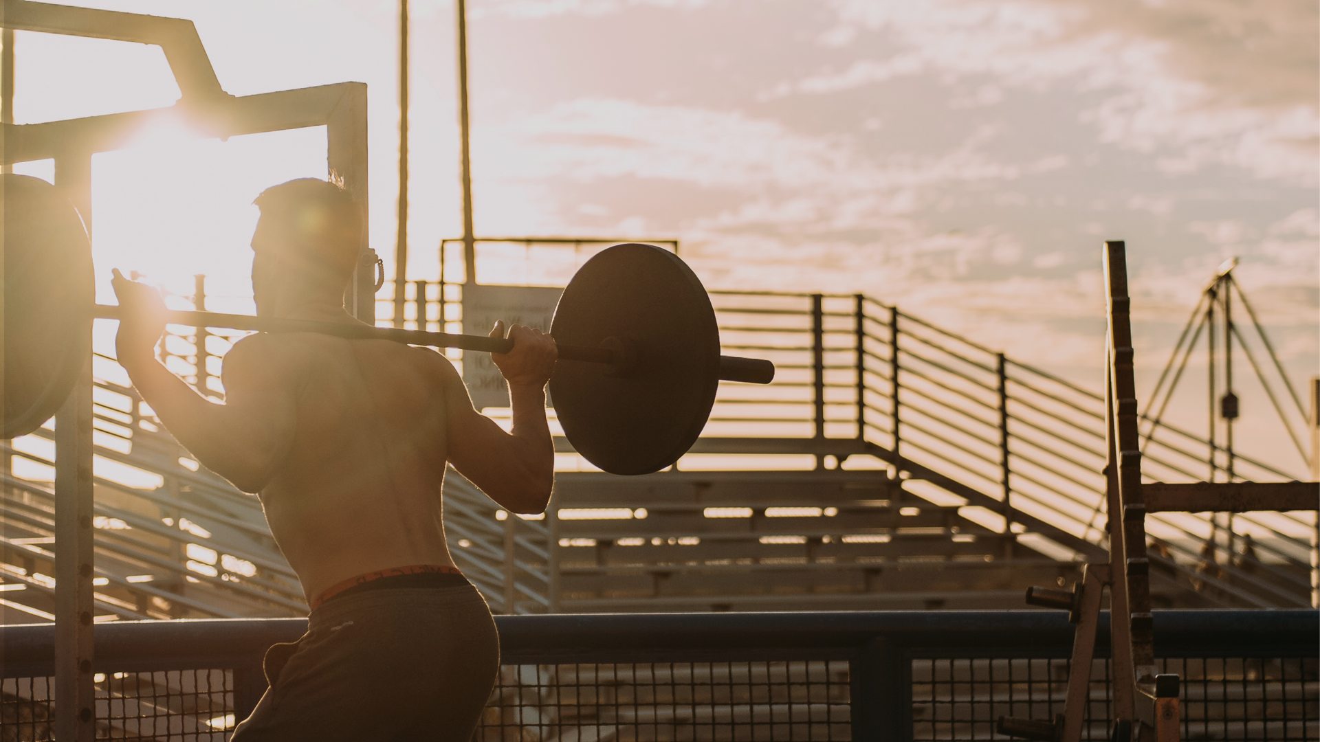 Athlete squatting a barbell at an outdoor gym at sunset