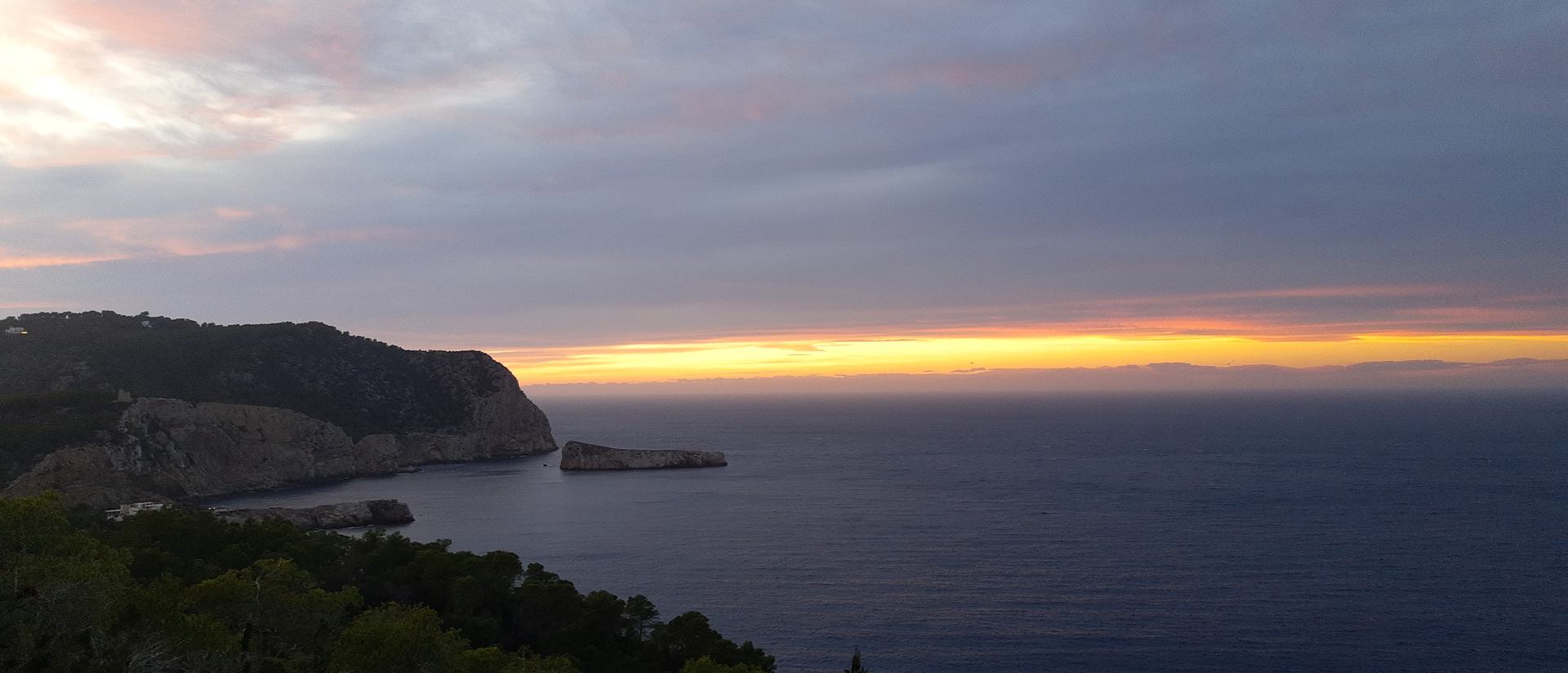 Sunset over the sea from the west coast of Ibiza, a headland and small islets in silhouette