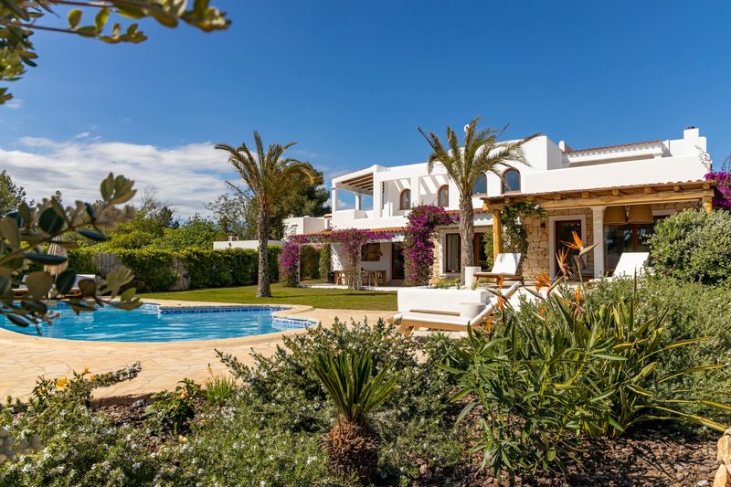 The white villa and its pool, with palms and pink flowers