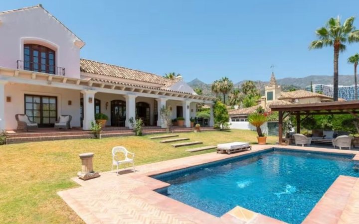 A white villa with a terracotta roof, a lawn, palm trees and a pool, in the hills near Marbella
