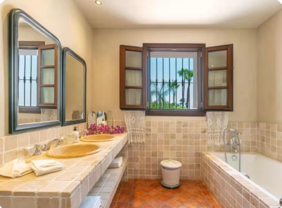 Stone-tiled bathroom with double basins and palm views from the window
