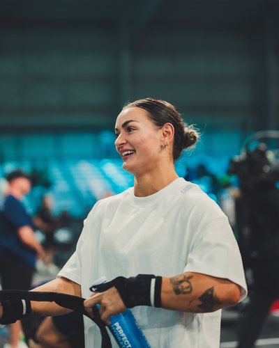 Kyra Milligan in a white T-shirt, smiling, with an arena behind her