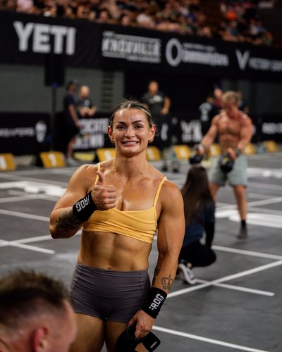 Kyra Milligan giving a thumbs up on a competition floor, a crowd behind her